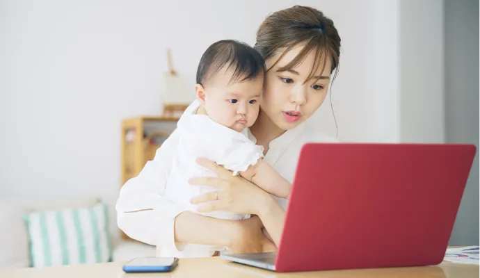 子供を抱きながらパソコンを見ている女性の画像