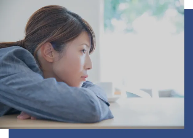 テーブルにうつ伏せて悩んでいる女性の画像